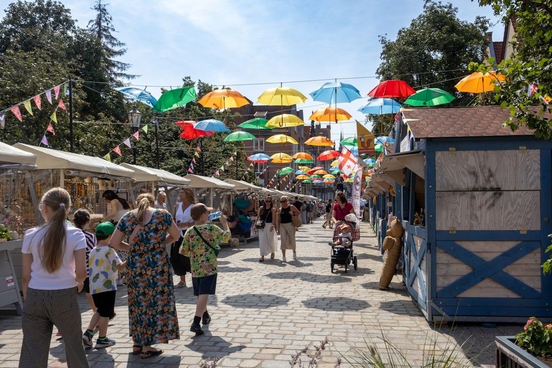 Gezinnen wandelen langs kraampjes onder kleurrijke paraplu’s op een markt