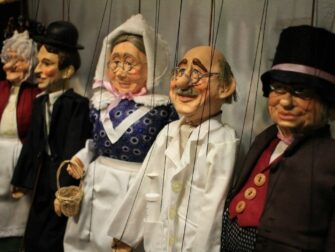 Rij aangeklede marionetten met zichtbare touwtjes in een poppentheater